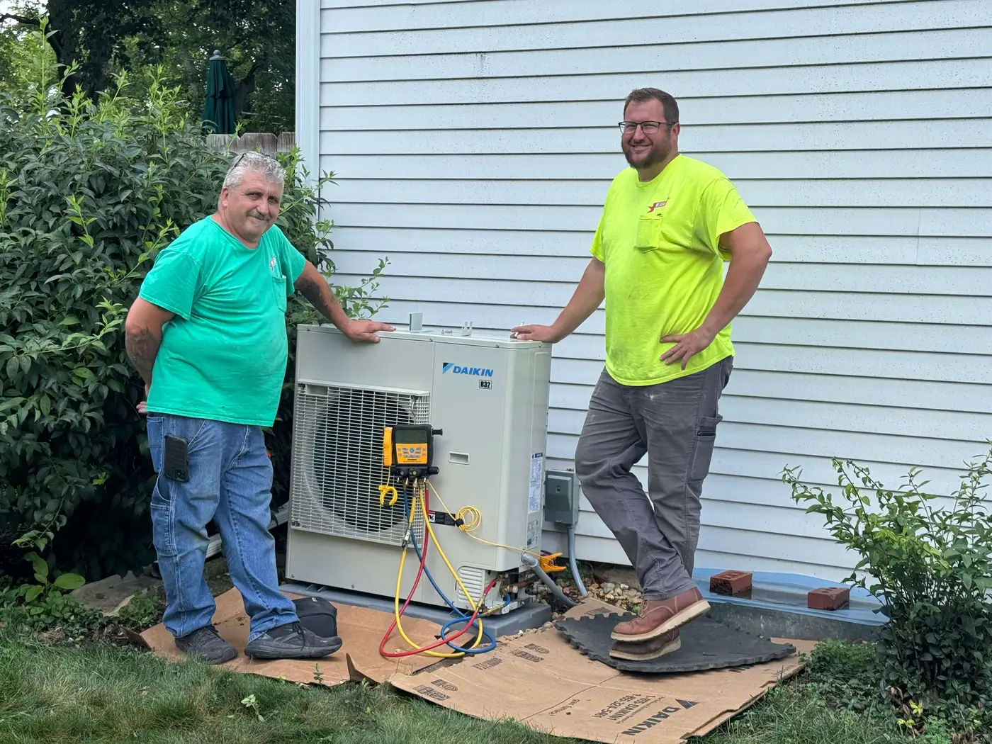 Two Allied technicians standing beside a freshly installed Daikin heat pump outside a Springfield home