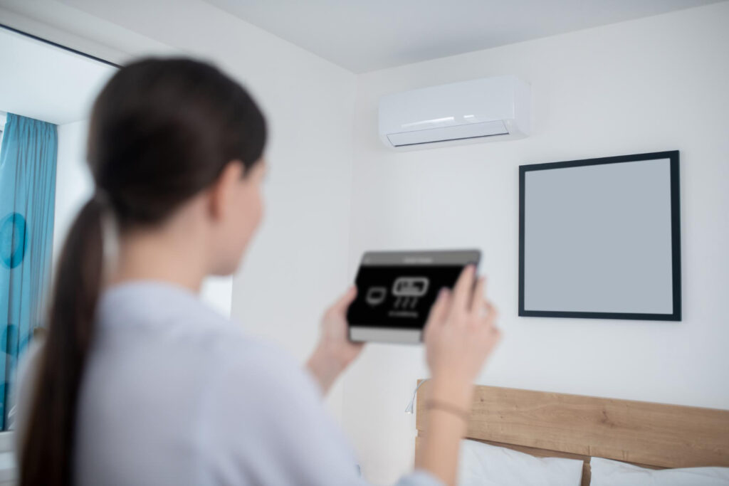 Smart Thermostat Connection Issues: How to Restore Wi-Fi Functionality in Sherman 1 Woman using a tablet to control a wall-mounted air conditioning unit in a modern bedroom setting.