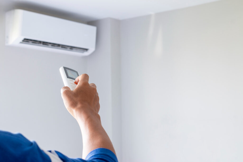 Why Your AC Is Running But Not Cooling Your Home in Springfield 2 Person using remote control to adjust a wall-mounted air conditioning unit in a home setting, illustrating HVAC system operation and maintenance.